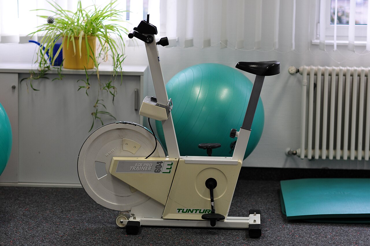 Sideprofil af ergometercykel med lille transporthjul under den forreste stelstang ved flywheel